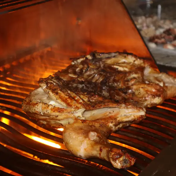 Whole chicken grilling over glowing coals